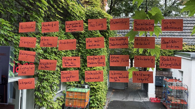 Ergebnisse des NEGZ-Workshops: rote Karten mit Schlagworten zur Datenkultur kleben an einer Glasscheibe, im Hintergrund begrünte Hauswand.